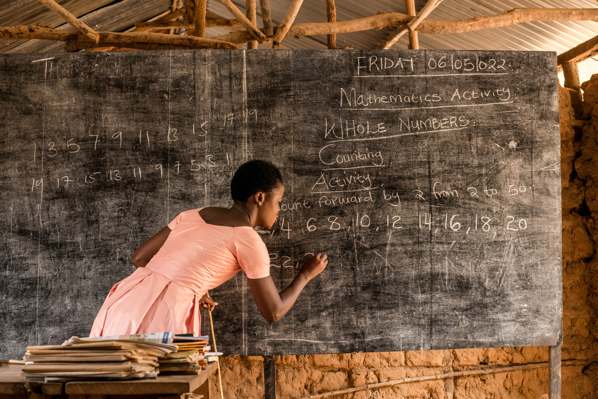 Ragazza di spalle con vestito rosa scrive su una lavagna