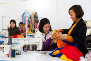 Gruppo di donne del vietnam sedute di fronte alle macchine da cucire durante una lezione di sartoria con insegnante