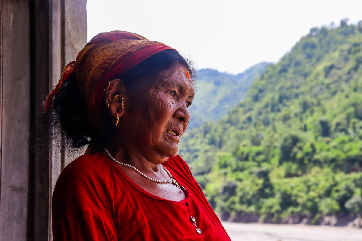 Primo piano di Nanimaya, donna del nepal, vestita di rosso guarda i suoi terreni allagati dall'alluvione
